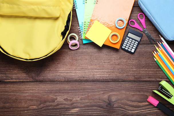 Yellow backpack with school supplies on brown wooden table - Foto, imagen