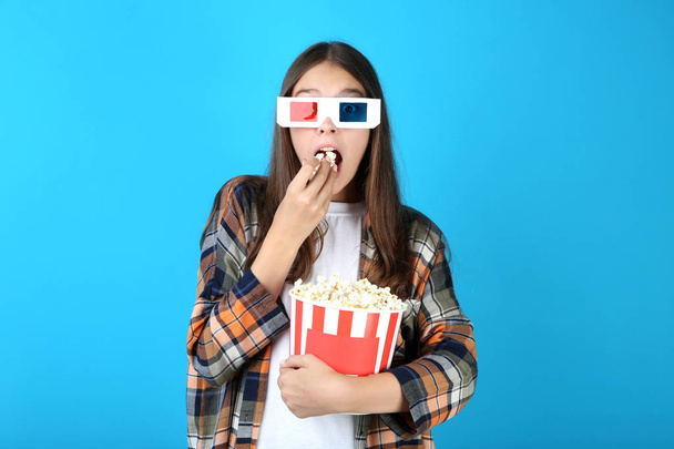 Young girl holding bucket with popcorn on blue background - Foto, imagen