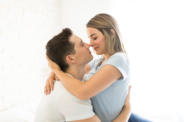 Vista lateral de una pareja apasionada a punto de besarse en un dormitorio iluminado
 - Foto, imagen