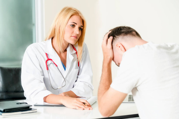 Femme médecin parle à un patient masculin sérieux dans le bureau de l'hôpital. Soins de santé et services médicaux
. - Photo, image