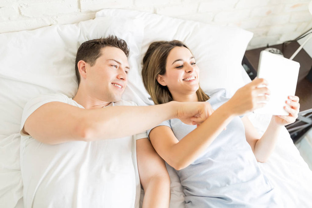 Высокоугольный вид мужчины и женщины с цифровым планшетом, лежащим в постели дома
 - Фото, изображение