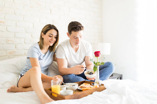 Мужчина и женщина едят здоровый завтрак, сидя на кровати в квартире
 - Фото, изображение