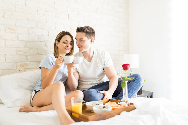 Amantes multiétnicos tazas de café mientras desayunan en la cama en casa
 - Foto, Imagen