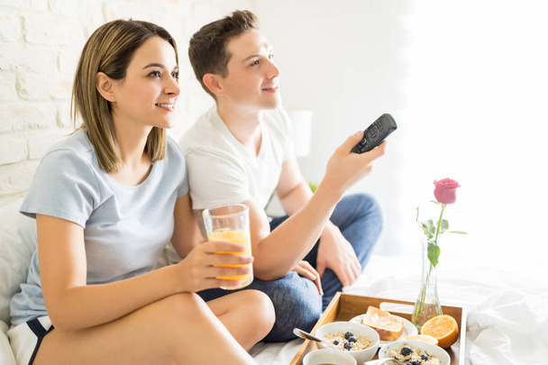 Содержательная пара завтракает во время просмотра телевизора на кровати дома
 - Фото, изображение