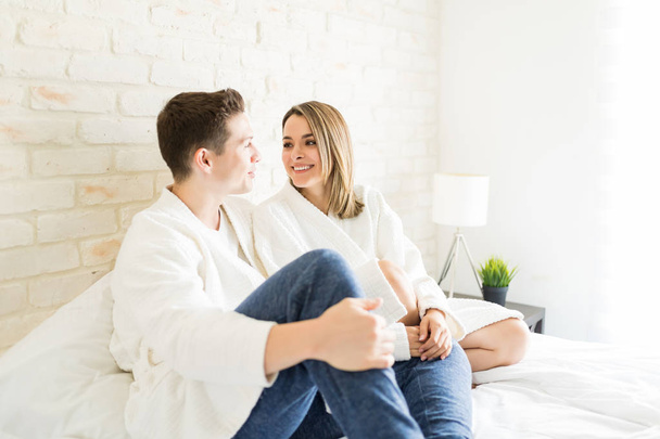 Ευτυχισμένο ζευγάρι στην αγάπη να μιλάμε, ενώ κάθεται στο κρεβάτι στο διαμέρισμα - Φωτογραφία, εικόνα
