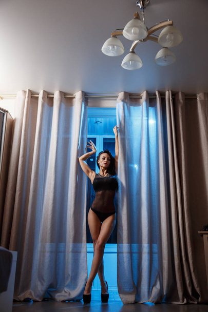 Shot of sexy brunette woman in black lingerie standing in hotel interior at nighttime  - Zdjęcie, obraz