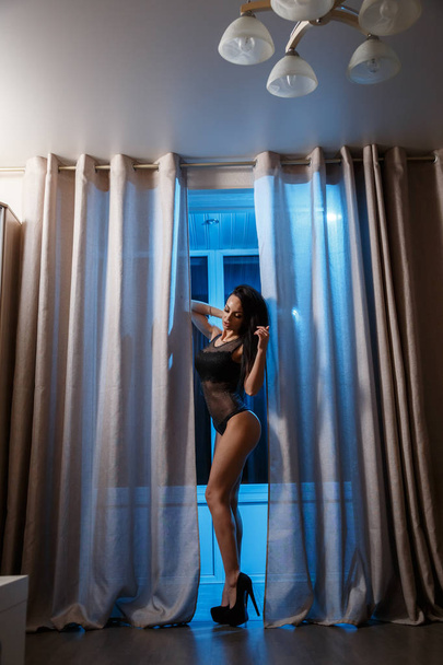 Shot of sexy brunette woman in black lingerie standing in hotel interior at nighttime  - Foto, afbeelding