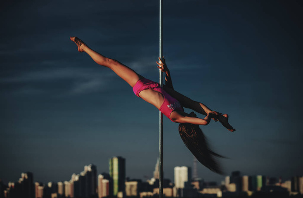 Young slim woman pole dancing on sky and city background. Dark dramatic colors. - Fotoğraf, Görsel