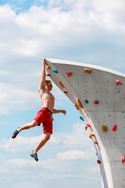 Photo of young sportive man hanging from top of climbing wall on summer - Fotografie, Obrázek
