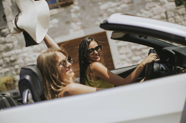 Young women with sunglasses driving her convertible top automobile on bright sunny day near sea - Photo, Image