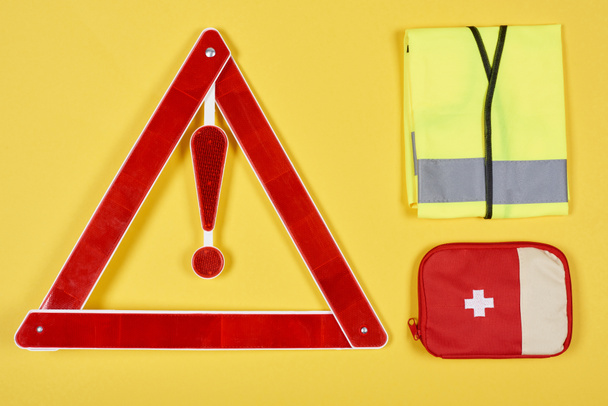 bovenaanzicht van waarschuwing driehoek verkeersbord, EHBO-kit en reflecterend vest geïsoleerd op geel - Foto, afbeelding