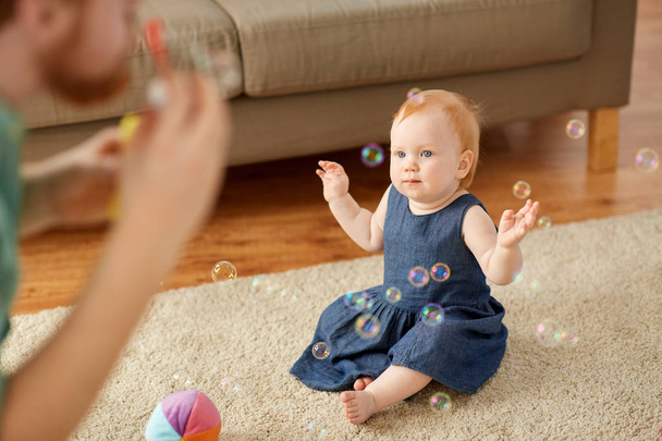 baby girl and father blowing soap bubbles at home - Foto, imagen