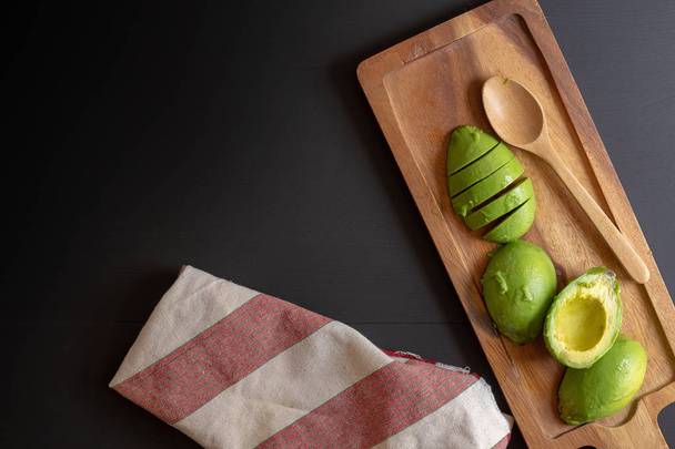 Fresh sliced organic avocado on black wooden background - Photo, Image