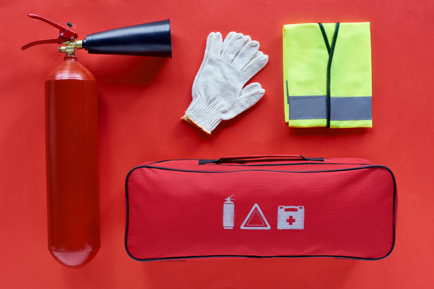 κάτοψη του αυτοκινήτου τσάντα, αντανακλαστικό γιλέκο, γάντια και πυροσβεστήρα σε κόκκινο φόντο - Φωτογραφία, εικόνα