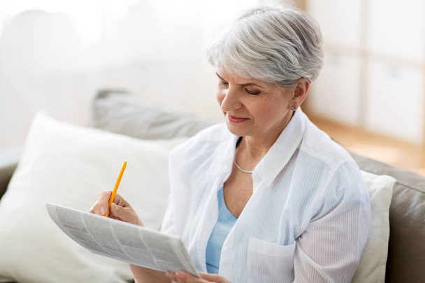 senior woman marking newspaper ad at home - Foto, afbeelding