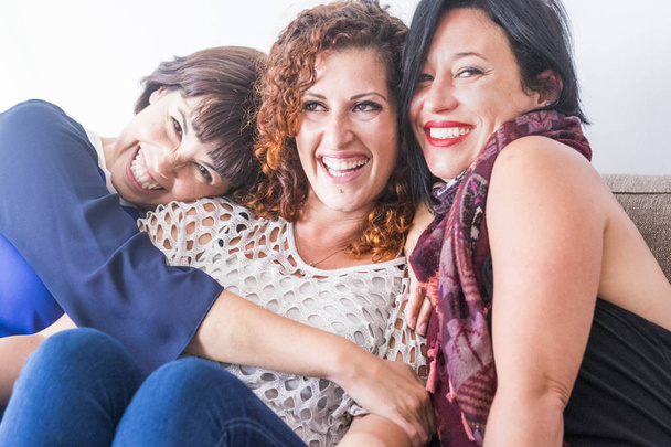 cheerful women sitting and hugging on sofa at home  - Foto, Bild