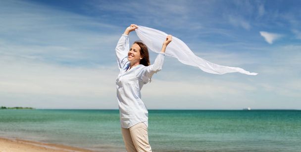 happy woman with shawl waving in wind on beach - Фото, изображение