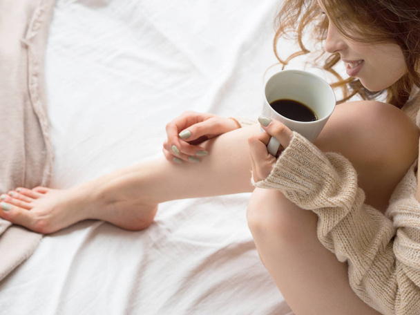 Foto de piernas y manos femeninas relajándose y bebiendo café en la cama
. - Foto, imagen
