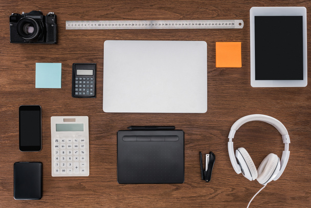 top view of workplace with laptop, ruler, photo camera, smartphone and digital tablet on wooden table  - 写真・画像