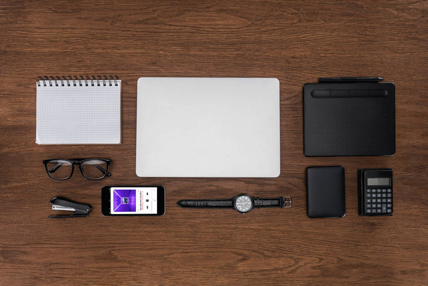 top view of workplace with arranged empty textbook, laptop, wristwatch and smartphone with apple music application on screen - 写真・画像