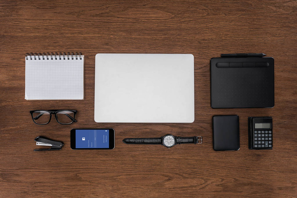 top view of workplace with arranged empty textbook, laptop, wristwatch and smartphone with facebok on screen - 写真・画像