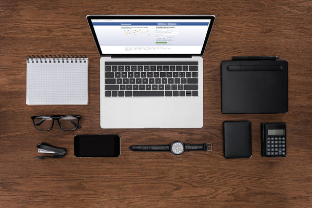 top view of workplace with arranged empty textbook, smartphone, wristwatch and laptop with facebook on screen - Fotó, kép