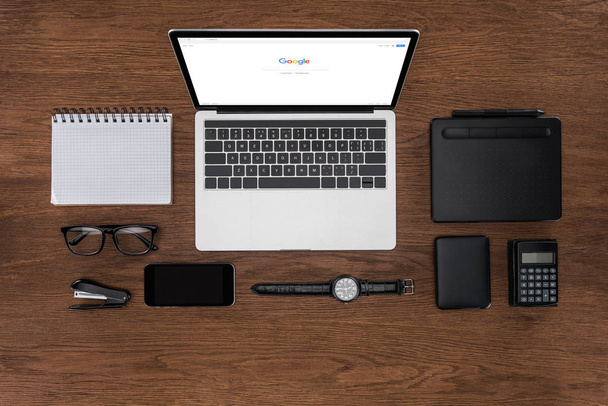top view of workplace with arranged empty textbook, smartphone, wristwatch and laptop with google on screen - Fotografie, Obrázek