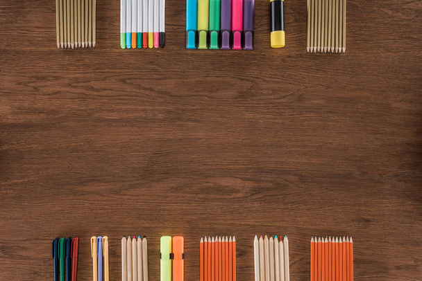 κάτοψη του τοποθετημένα πολύχρωμα μολύβια και μαρκαδόρους στο ξύλινο τραπέζι  - Φωτογραφία, εικόνα
