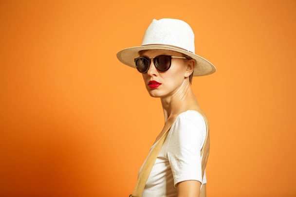 Fashionable woman in a hat and sunglasses, accessories, posing in studio over vibrant color background, copy space. Fashion summer or autumn photo - Foto, Imagen