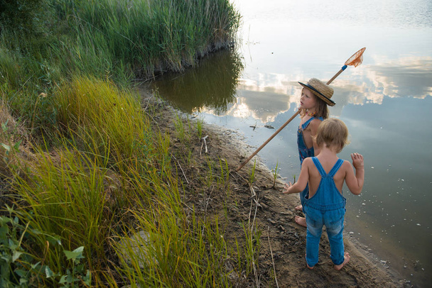 Двое детей с сеткой для бабочек у реки
 - Фото, изображение