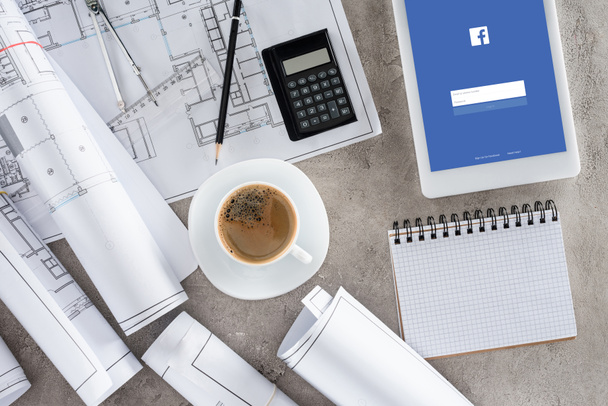 vista superior del lugar de trabajo del arquitecto con taza de café, planos, calculadora y tableta digital con facebook en pantalla
 - Foto, imagen