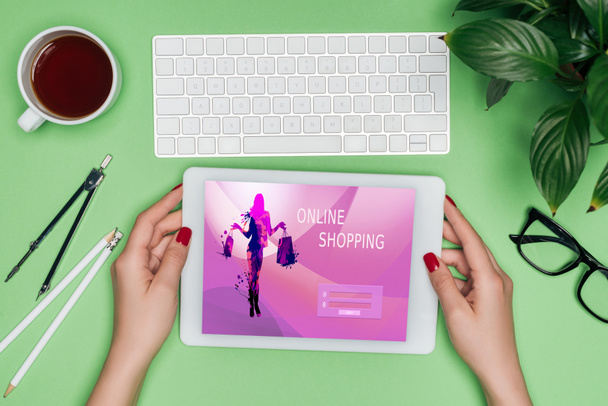 デジタル タブレットの画面で分周器、コーヒー、鉢植えの植物とテーブルでオンライン ショッピングを保持している女性の建築家のトリミングされた画像  - 写真・画像