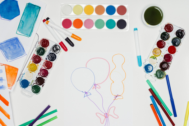 top view of artist workplace with colorful paints, markers and painting of air balloons on white table - Photo, Image