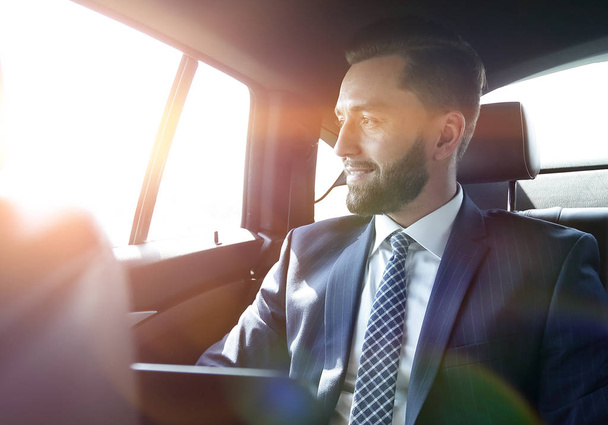 Smiling businessman with laptop sitting in car - Valokuva, kuva