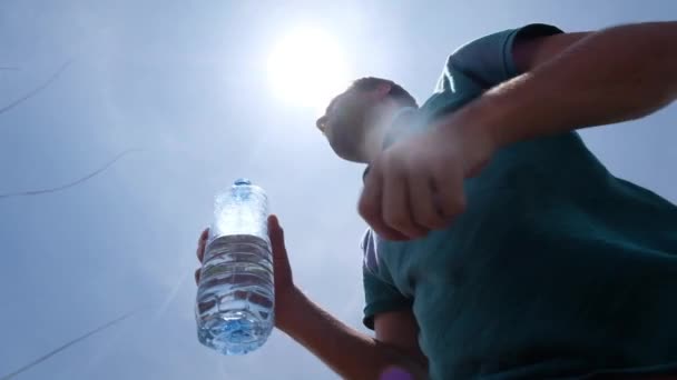 Молодий чоловік п'є пляшку води, що стоїть на відкритому повітрі в спекотне літо
 - Кадри, відео