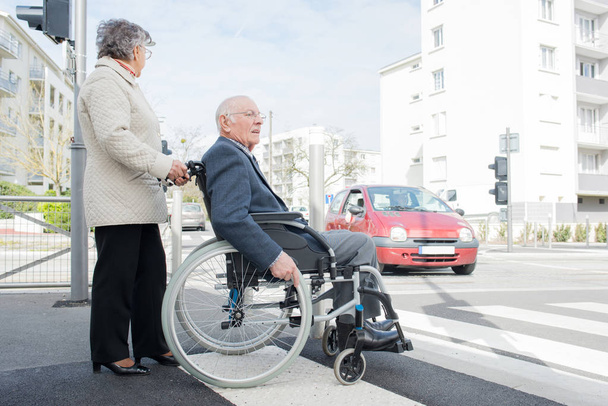 wife and elderly person in a wheelchair crossing the road - Valokuva, kuva