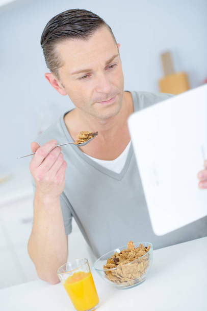 young man eating breakfast whilst using digital tablet - Foto, Imagen