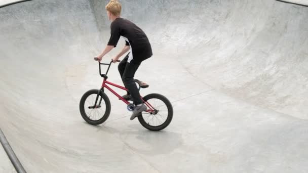 Um menino está montando BMX truques de ciclismo em um parque de skate em um dia ensolarado. Movimento super lento
 - Filmagem, Vídeo
