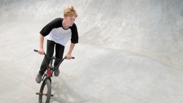 Un niño está montando trucos de ciclismo BMX en un parque de skate en un día soleado. Super cámara lenta
 - Imágenes, Vídeo
