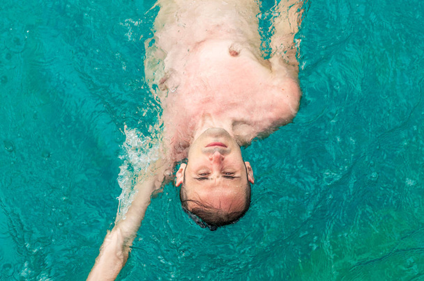 Top view of a young Caucasian man swimming back crawl in a swimming pool - Photo, Image