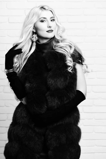 young fashionable sexy pretty woman with beautiful long curly blonde hair in waist coat of burgundy or red fur and black velvet gloves on brick wall studio background. - Fotoğraf, Görsel