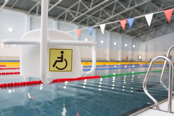 Elevador para a descida de pessoas com deficiência para a piscina. Em um fundo embaçado, uma piscina é visível
 - Foto, Imagem