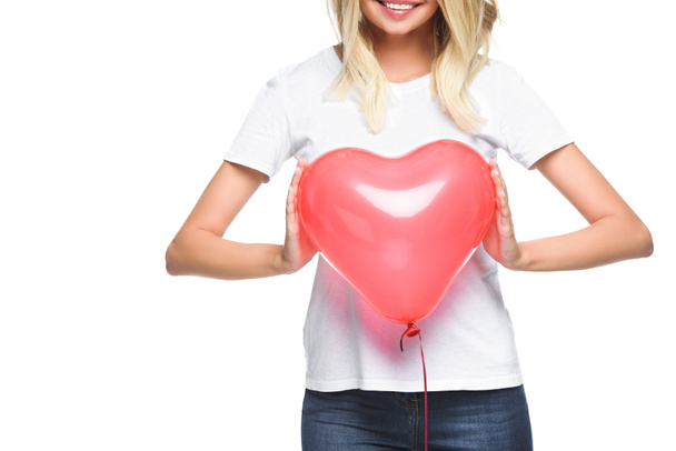 cropped image of smiling girl in white shirt holding heart shaped balloon isolated on white - Fotó, kép