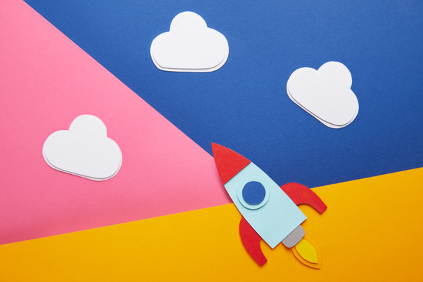 bovenaanzicht van wolken en kleurrijke raket op achtergrond creatief papier - Foto, afbeelding