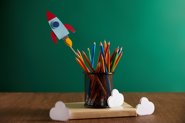 colorful pencils, rocket, clouds on book with chalkboard on background - Фото, изображение
