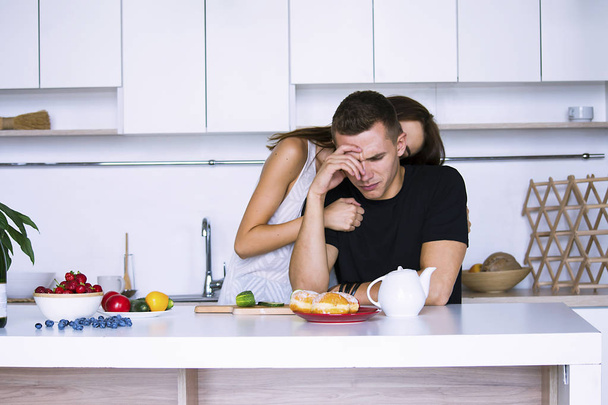 pretty woman calms a man in a white kitchen - Foto, afbeelding