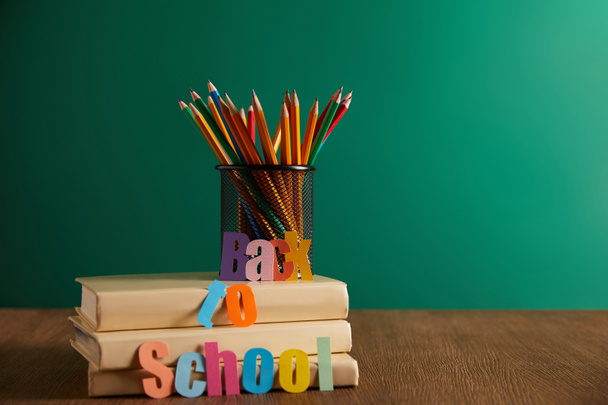 colorful pencils on books with back to school lettering, chalkboard on background - Foto, imagen