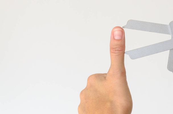 Close-up de polegar estendido sendo medido com um instrumento de metal contra um fundo branco
 - Foto, Imagem