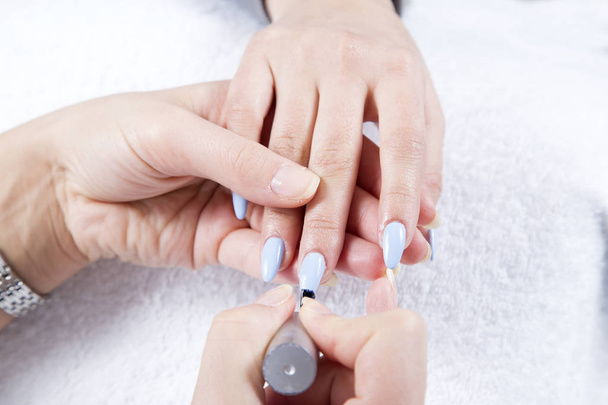 Nail Beautician Applying Light Blue Nail Polish To Fingernails At Beauty Salon Closeup - Фото, изображение