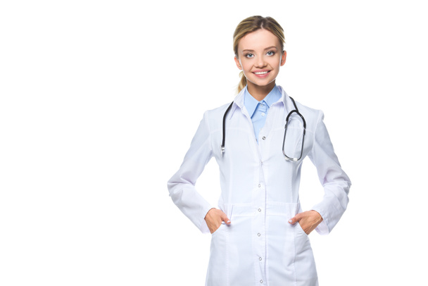 junger lächelnder Arzt in weißem Mantel mit Stethoskop, isoliert auf weiß - Foto, Bild